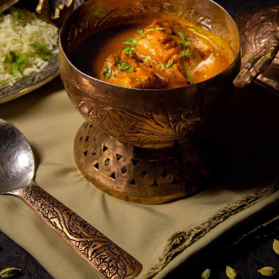 Rogan josh in an engraved copper bowl beside Kashmiri rice